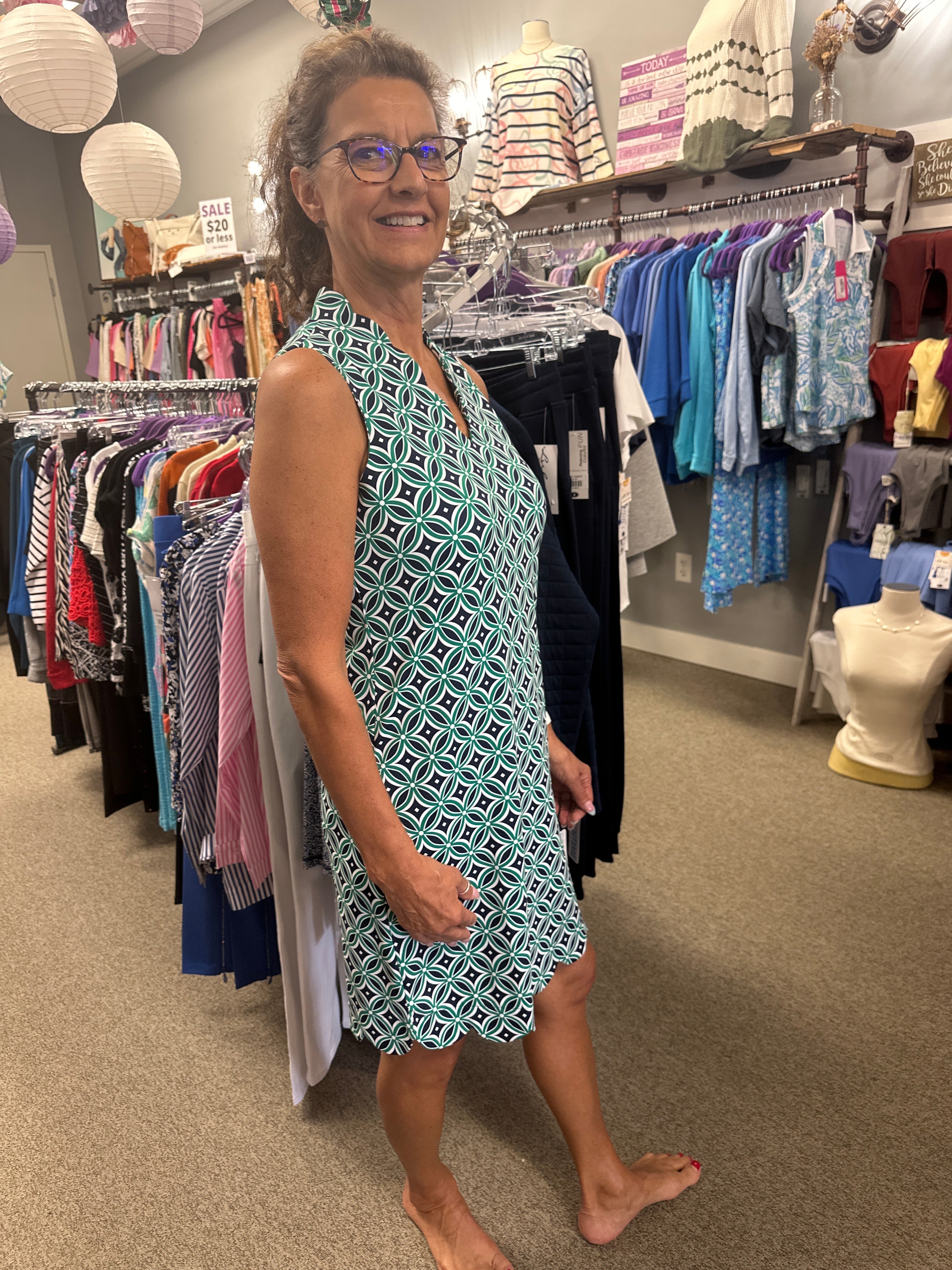 Person wearing a patterned dress standing in a clothing store with racks of clothes in the background.