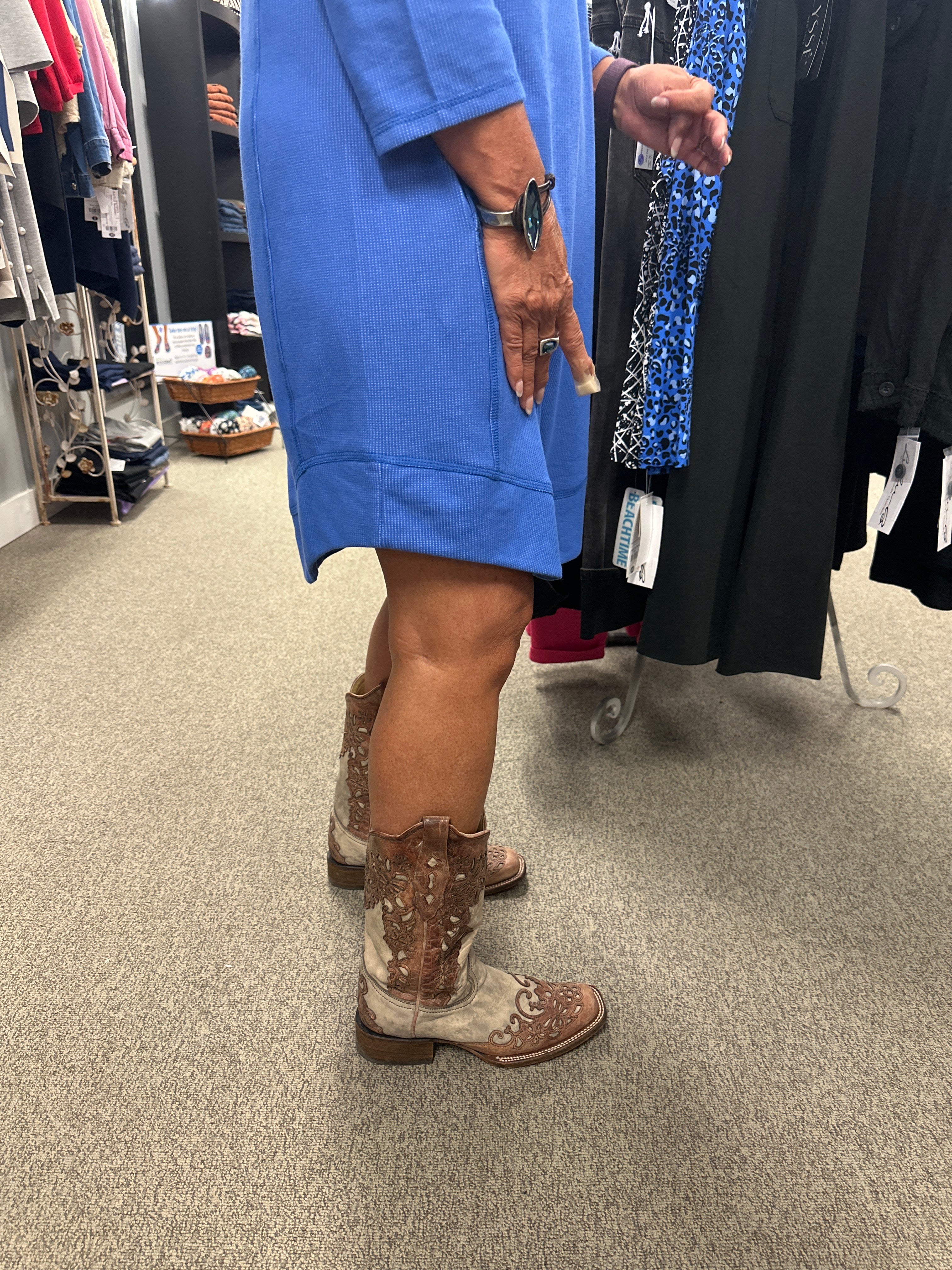 Person wearing a blue jacket and brown boots standing on a carpeted floor with clothing racks in the background.