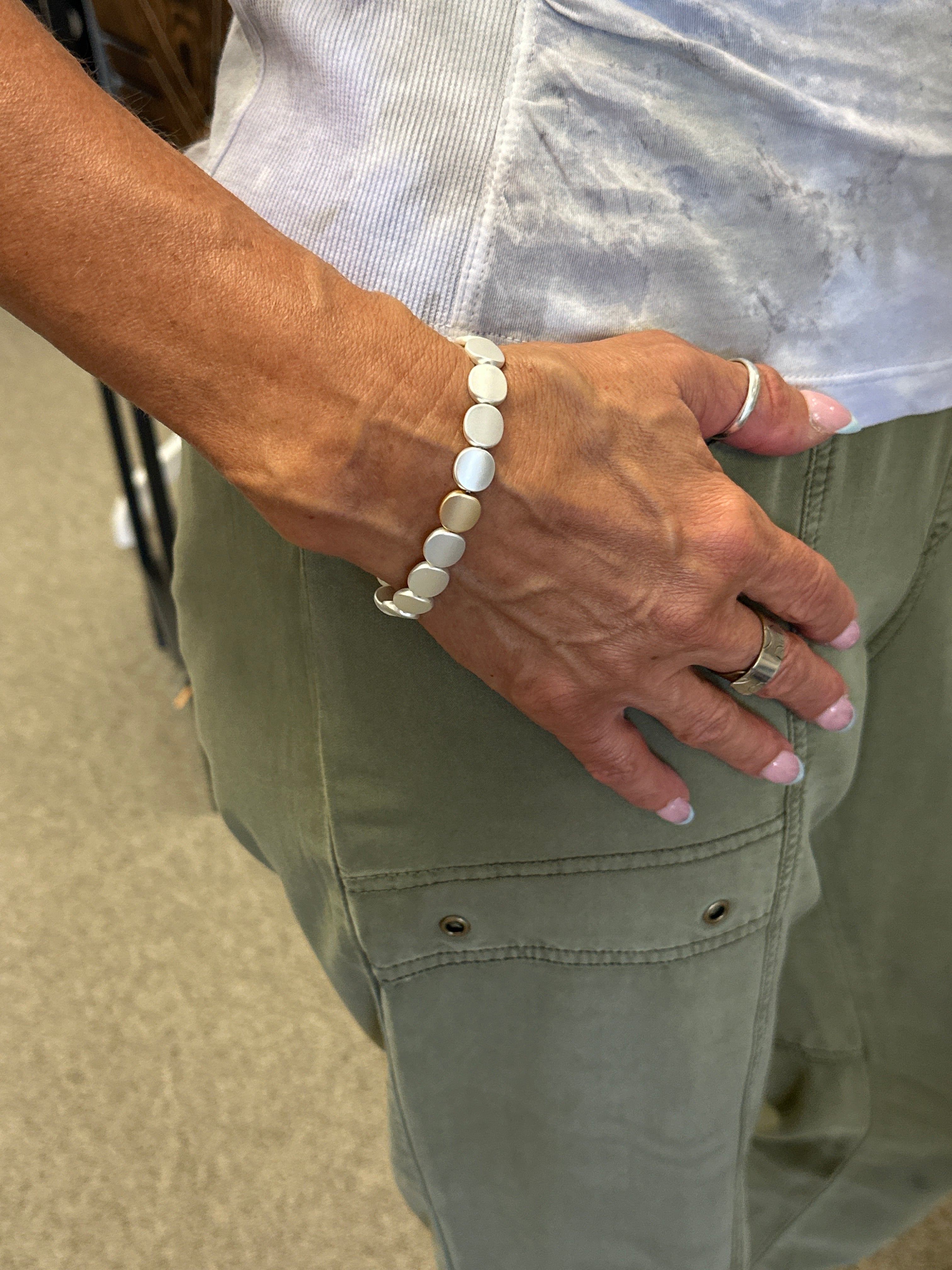 Hand wearing a bracelet on a person wearing a light-colored shirt and green pants.