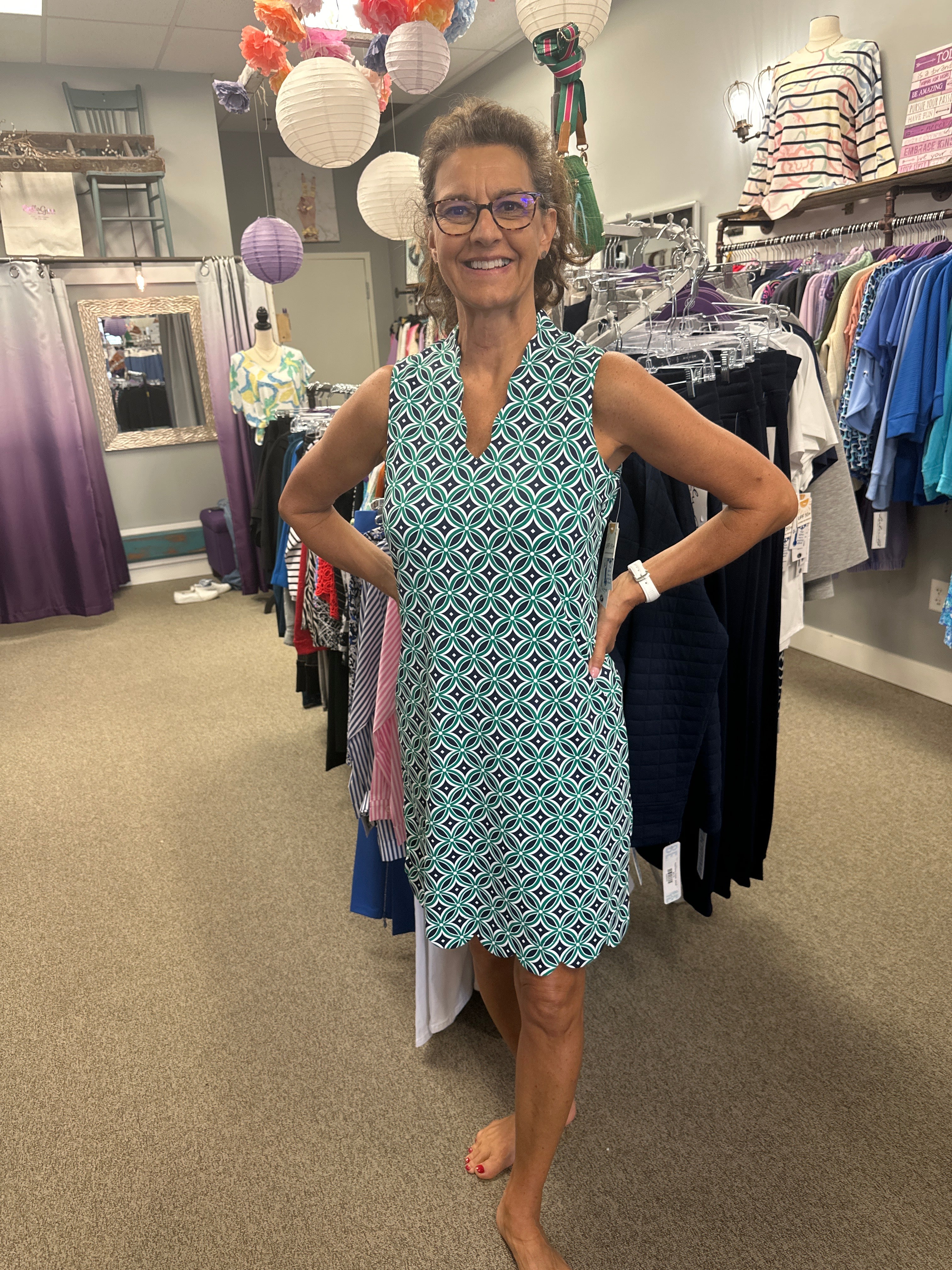 Woman in a patterned dress standing in a store with racks of clothes.