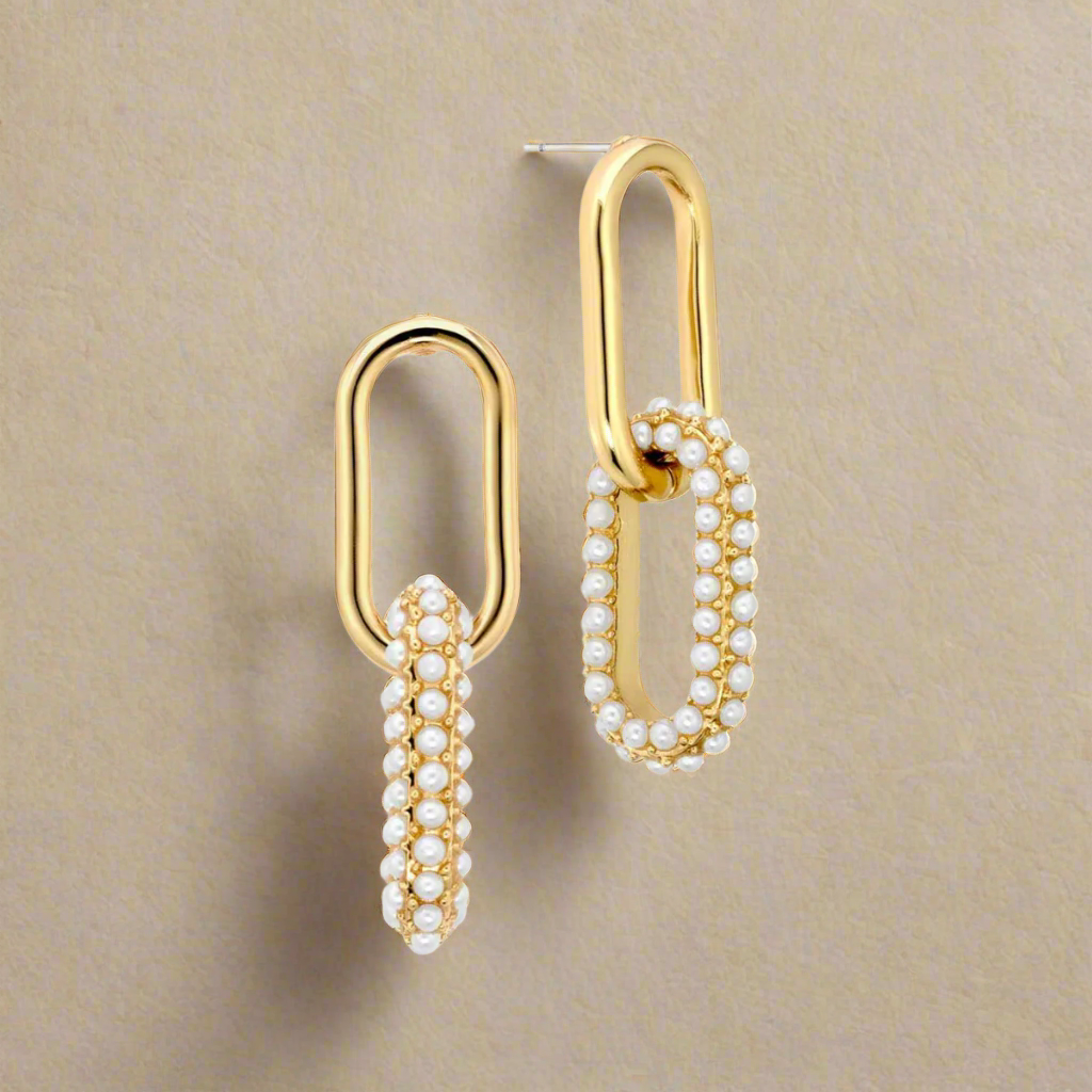 Gold earrings with pearl accents on a beige background