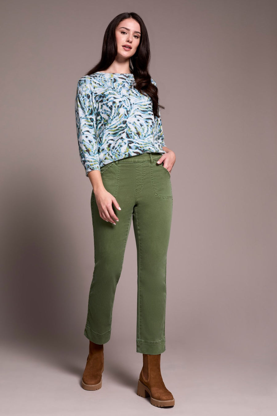 Woman wearing a patterned top and green pants against a plain background
