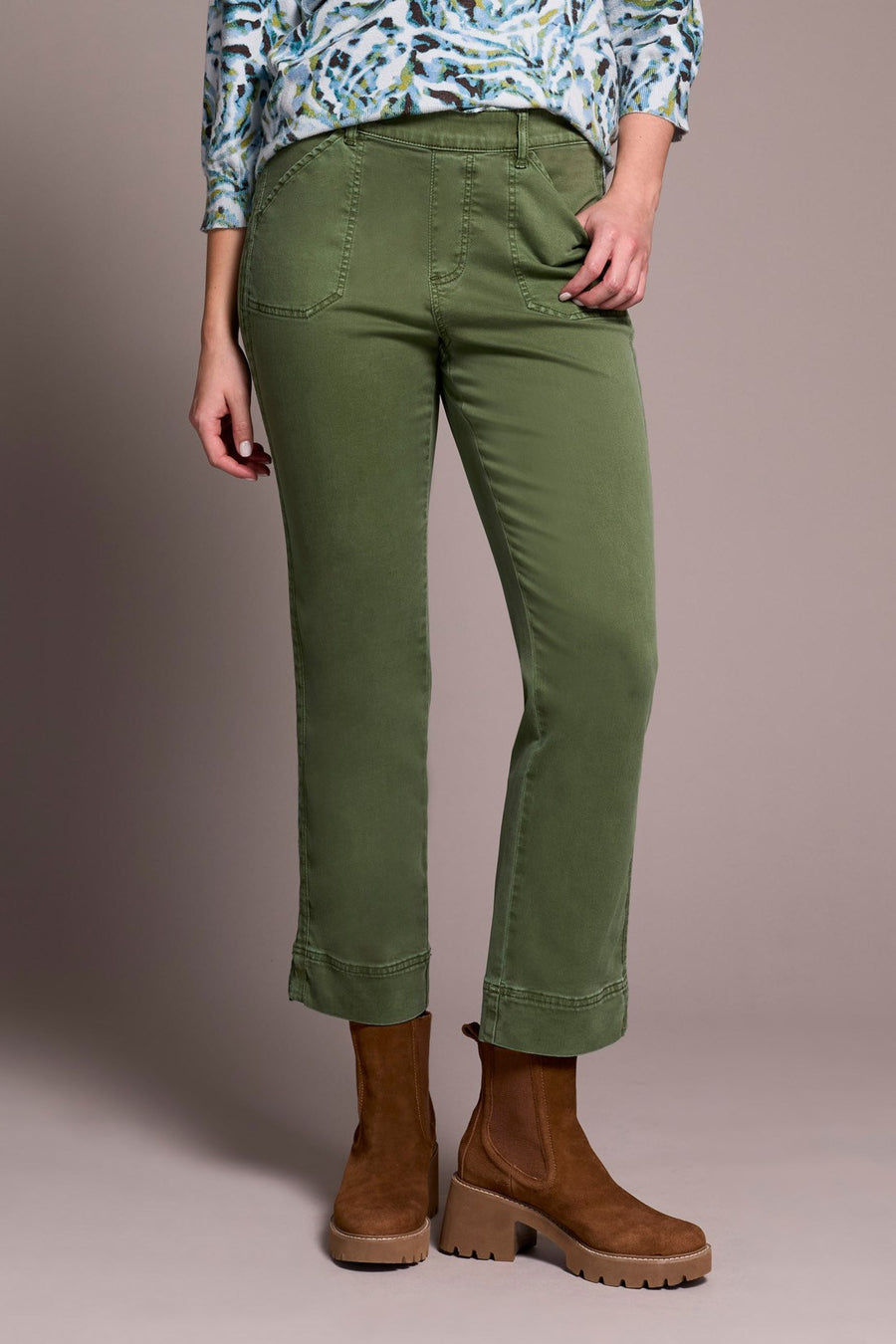 Person wearing green pants and brown boots against a neutral background