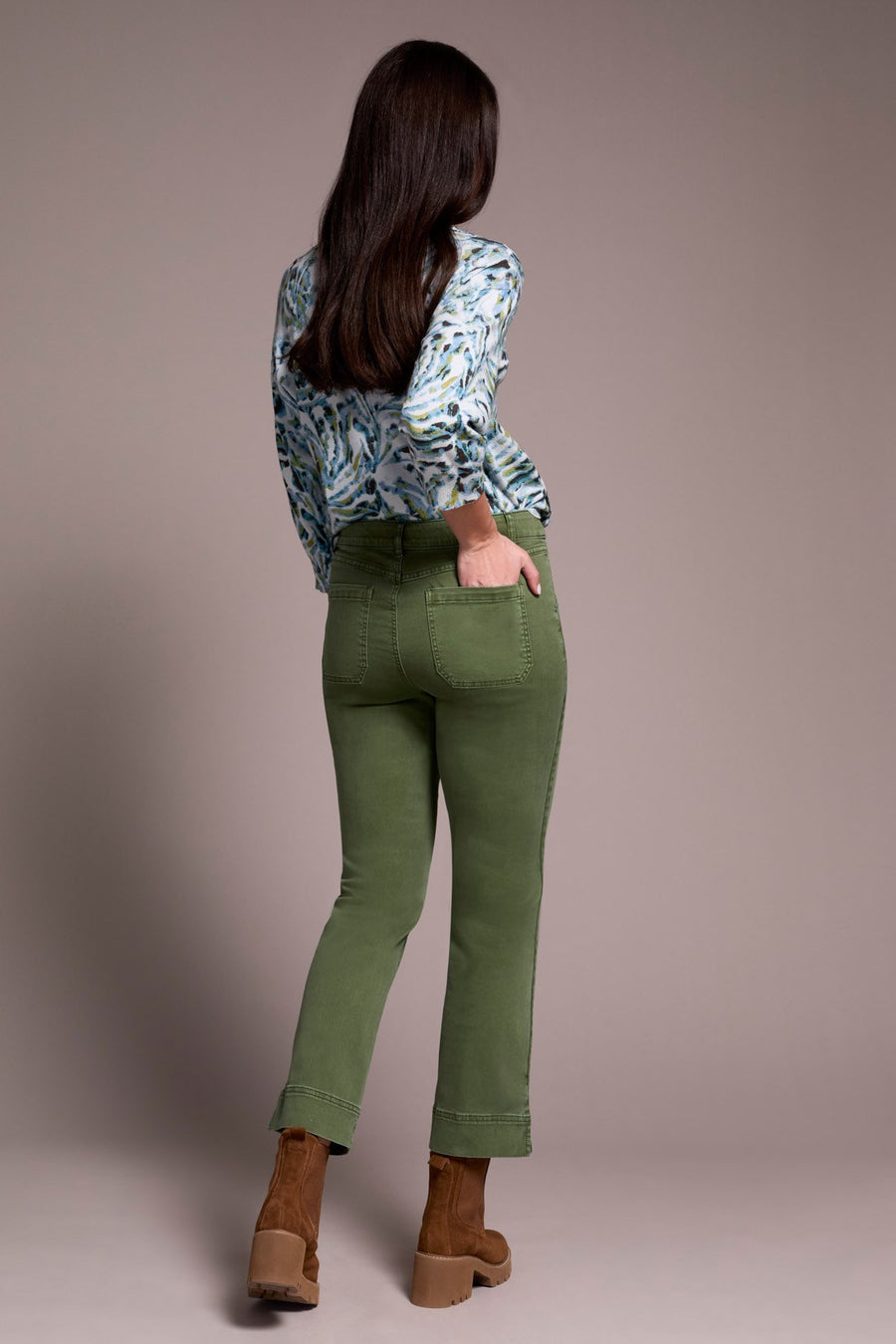 Woman wearing green pants and a patterned shirt against a plain background