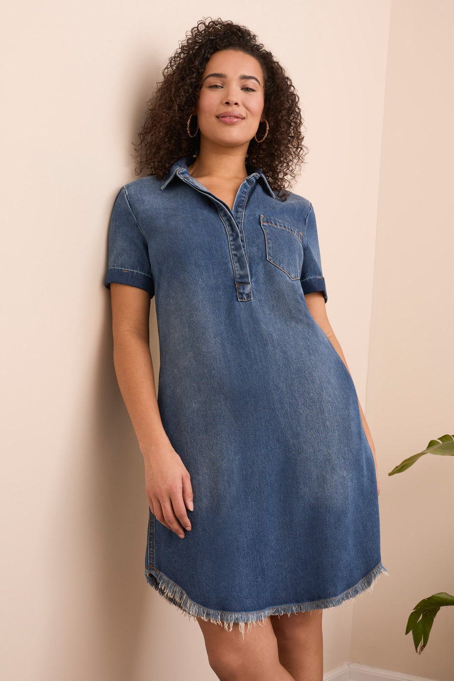 Woman wearing a blue denim dress against a beige wall