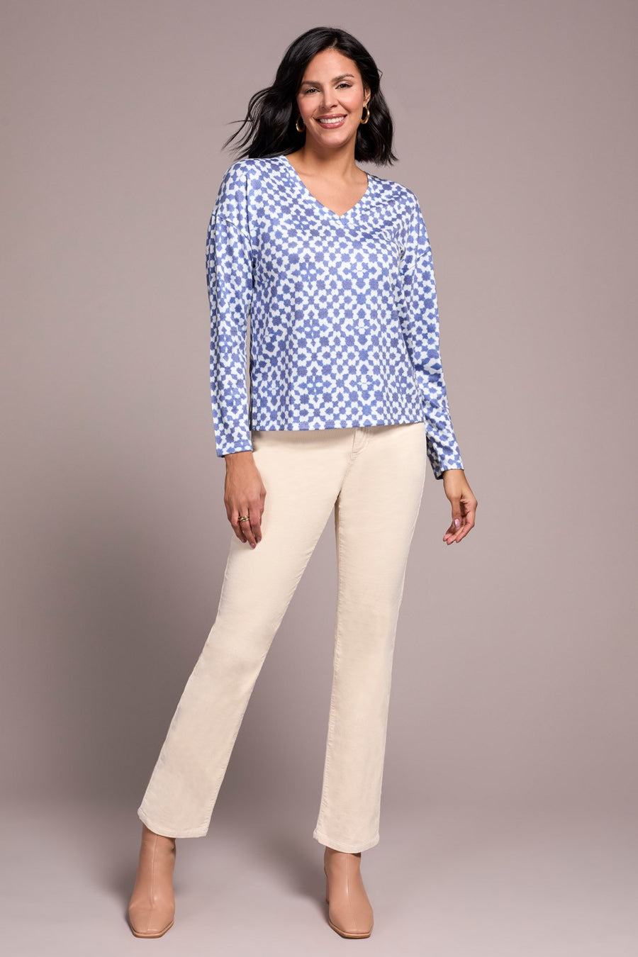 Woman wearing a blue patterned blouse and beige pants against a plain background