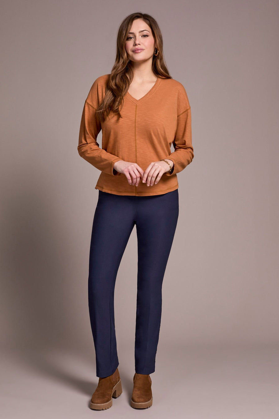 Woman wearing an orange top and navy pants against a plain background